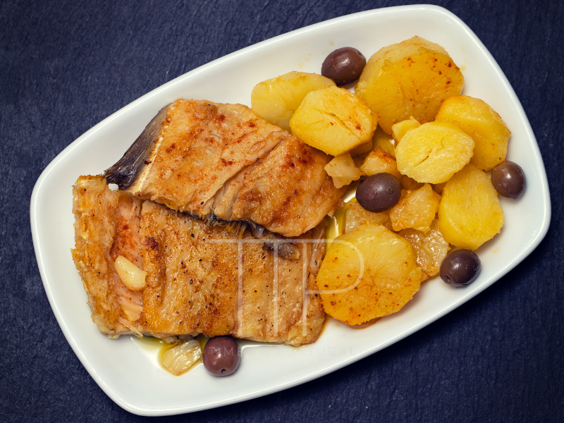 white plate with fish, potatoes and olives
