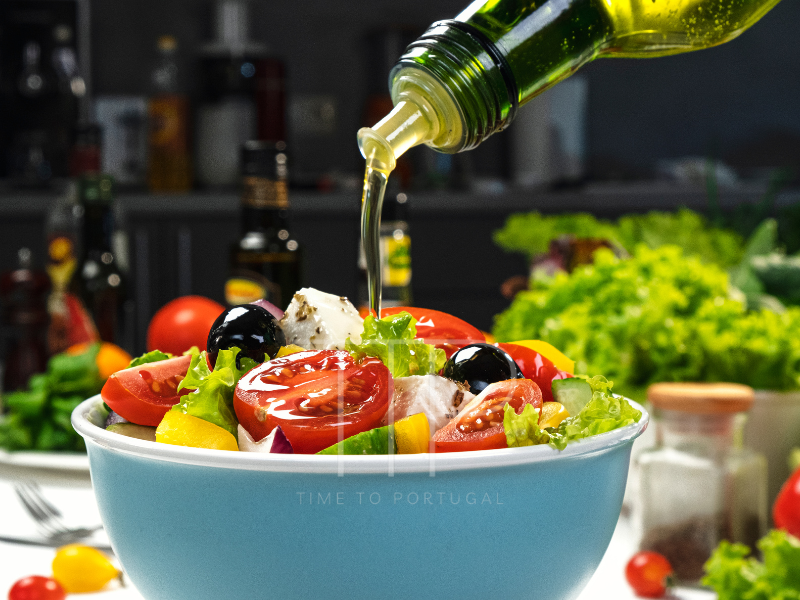 Olive oil pouring out of a bottle onto mixed salad in a white bowl